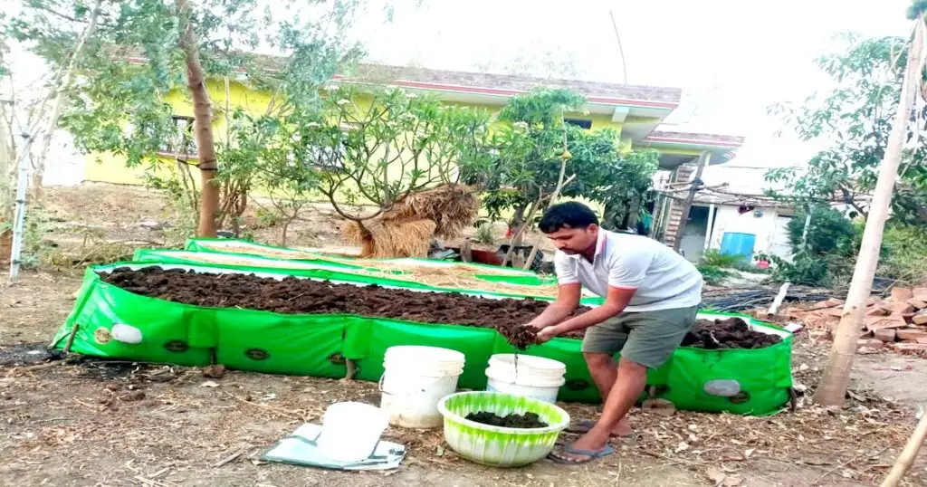 A man inspecting dark organic vermicompost with his hands from a green portable HDPE composting bed in a rural backyard farming setup